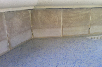 A corner of a drained pool with tiles and a blue floor with a drain