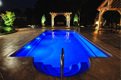 A night photograph of a rectangular pool lit up with blue lights